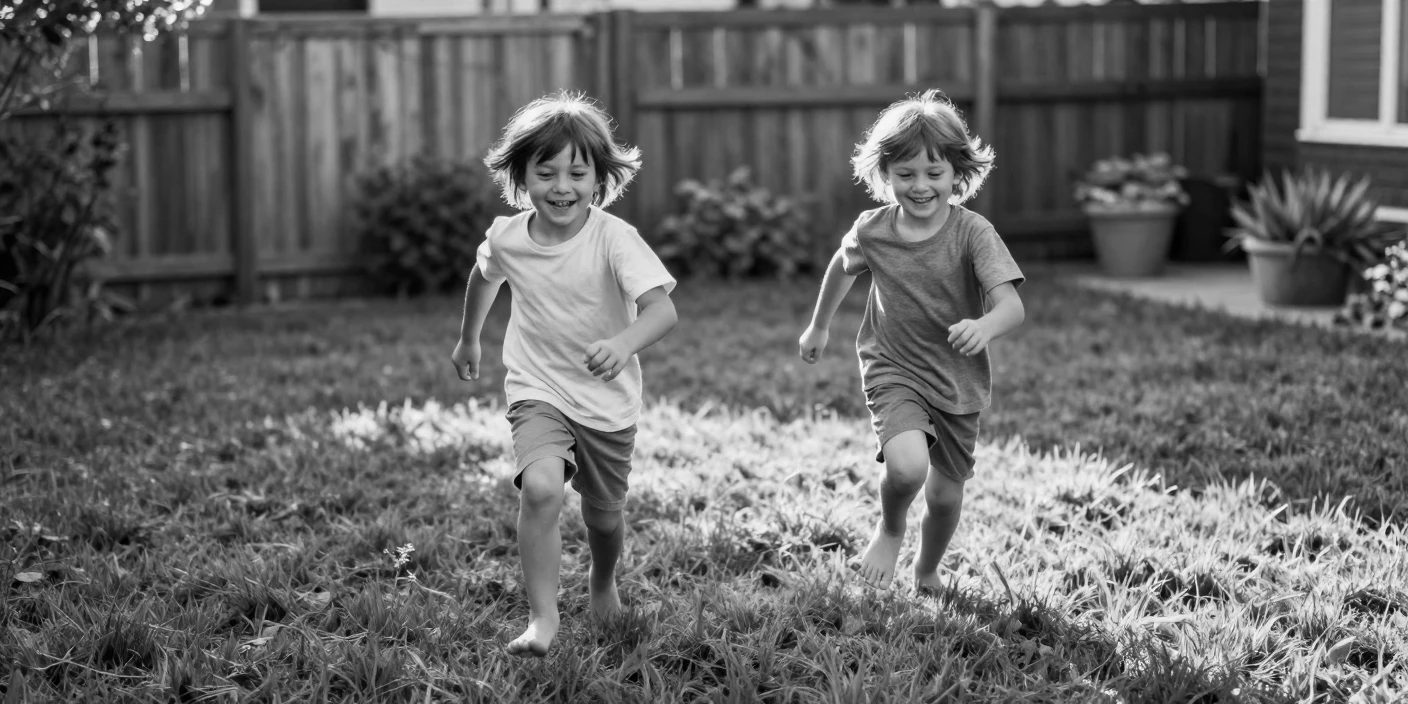 A pair of twins chase each other across the lawn on a grassy backyard lawn.