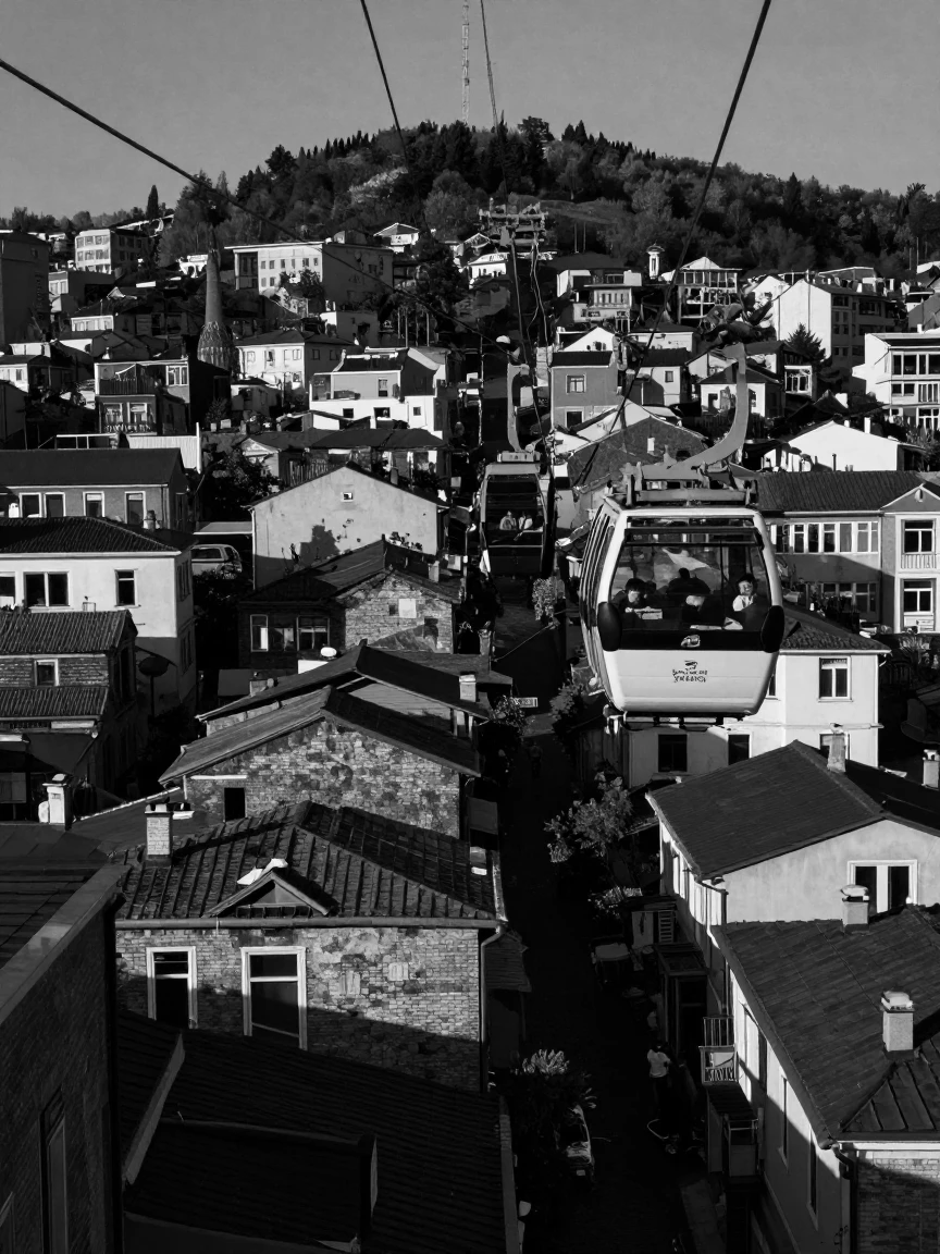 A gondola cable car carries passengers above a hillside city over rooftops toward a distant summit.