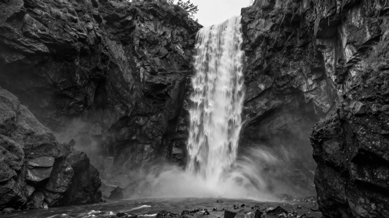 A towering waterfall crashes into a misty gorge below through a steep canyon.