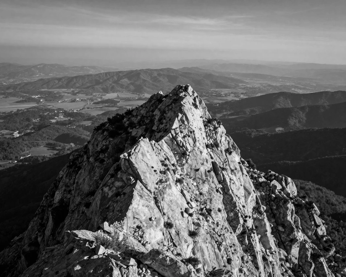 A rocky mountain summit towers silently over a distant valley overlooking a vast green valley.