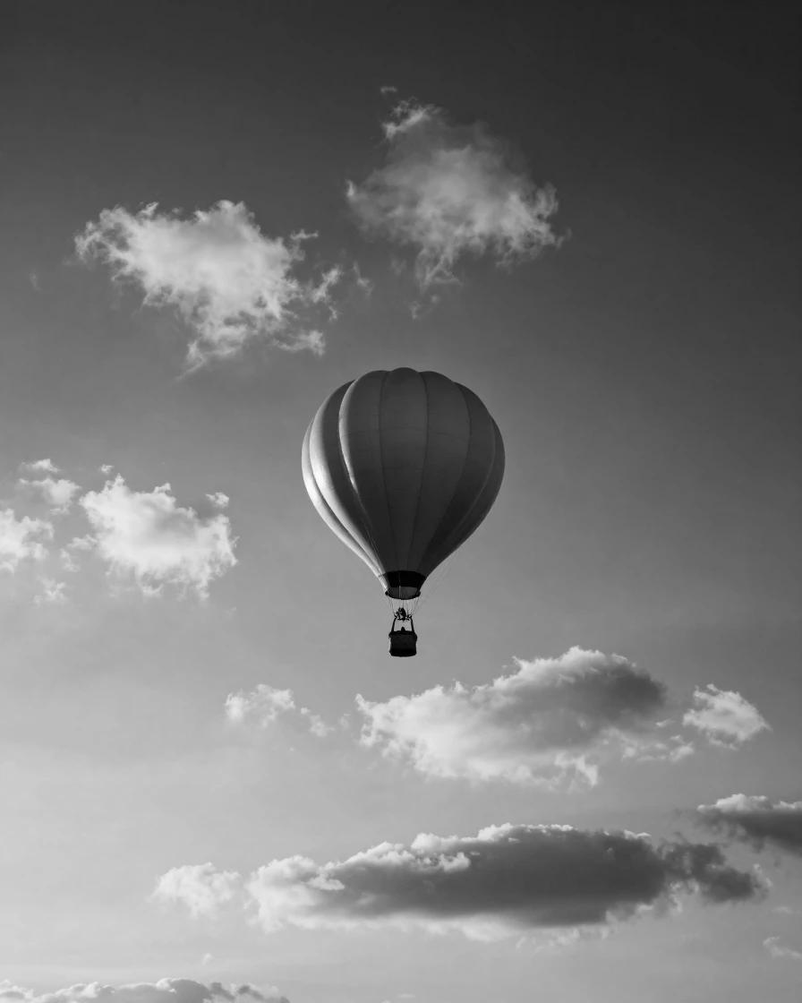 A weather balloon rises through scattered clouds into a pale morning sky.