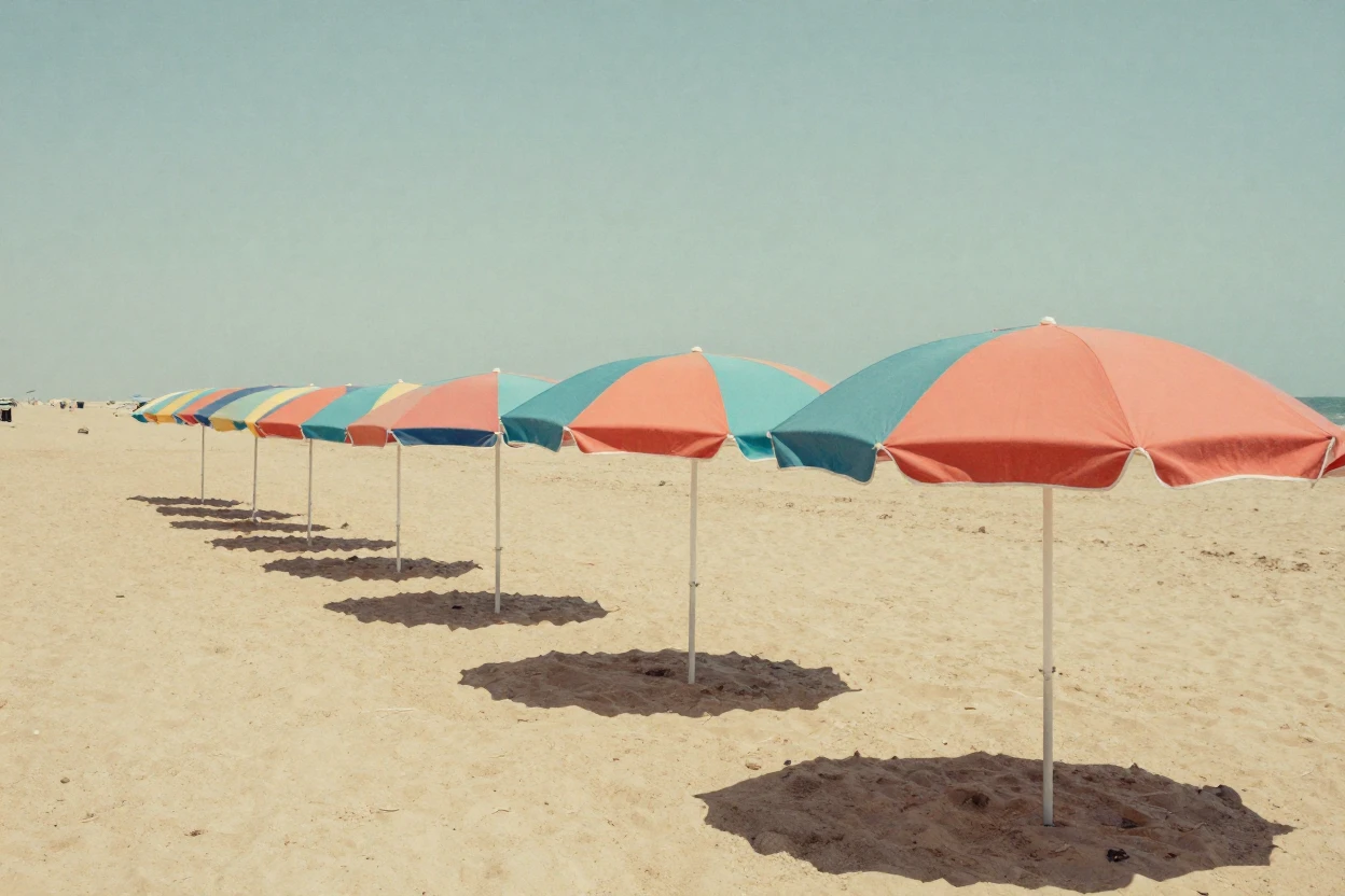 A row of colorful beach umbrellas along a sandy shore, under harsh midday sun, in still, windless air, in summer, in vivid coral and turquoise hues, from a slightly elevated vantage point.